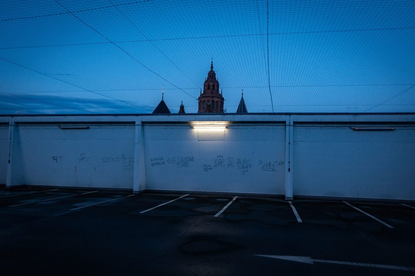 Mainzer Dom St. Martin Dunkler Dachparkplatz. Lediglich ein Parkplatz ist beleuchtet und direkt darüber die Silhouette des Mainzer Doms vor dem Himmel.