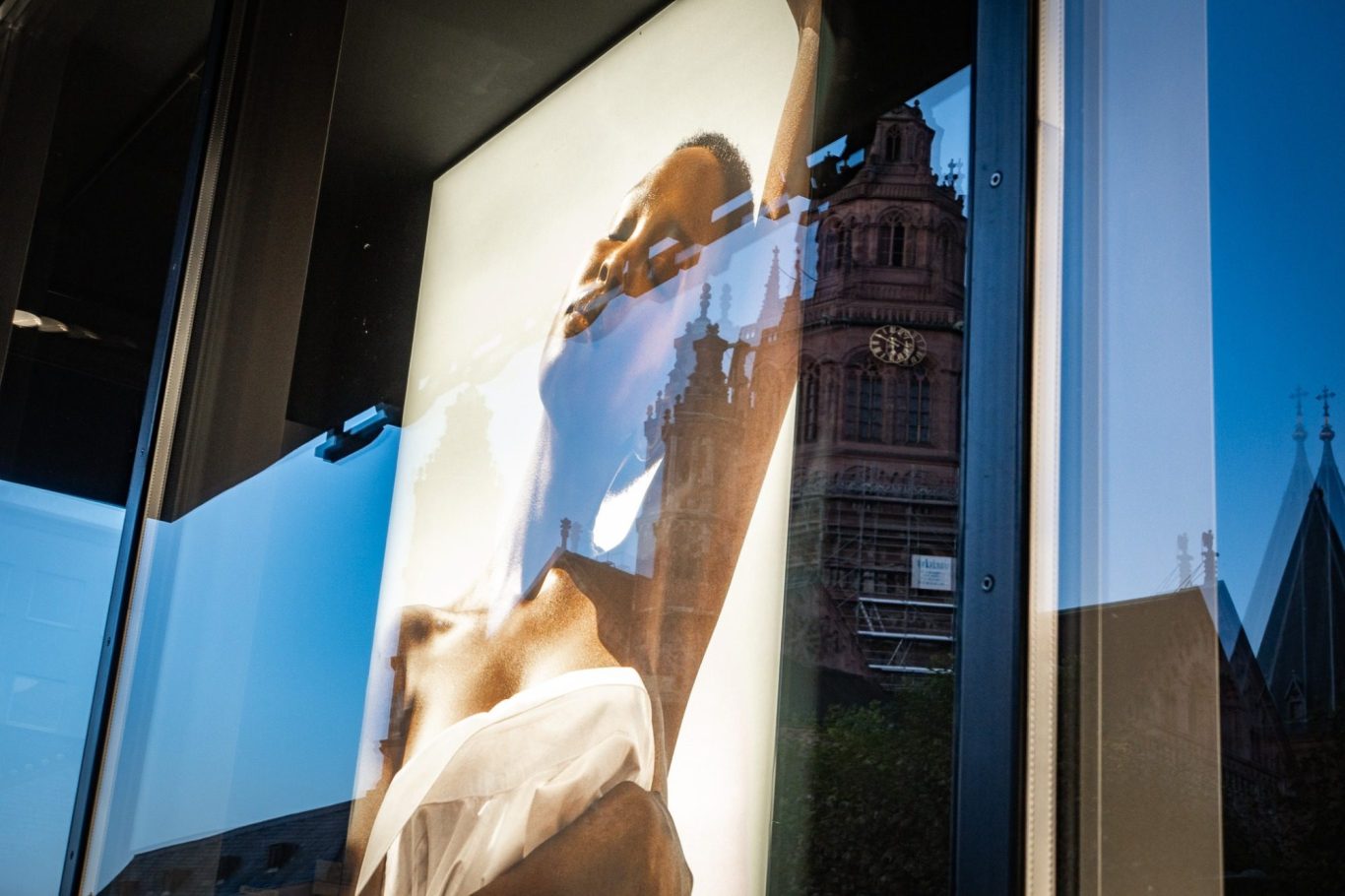 Mainzer Dom St. Martin, Douglas am Höfchen Frau in weißem Oberteil steht vor einem reflektierenden Schaufenster, sodass es aussieht, als würde sie sich an den Mainzer Dom schmiegen.