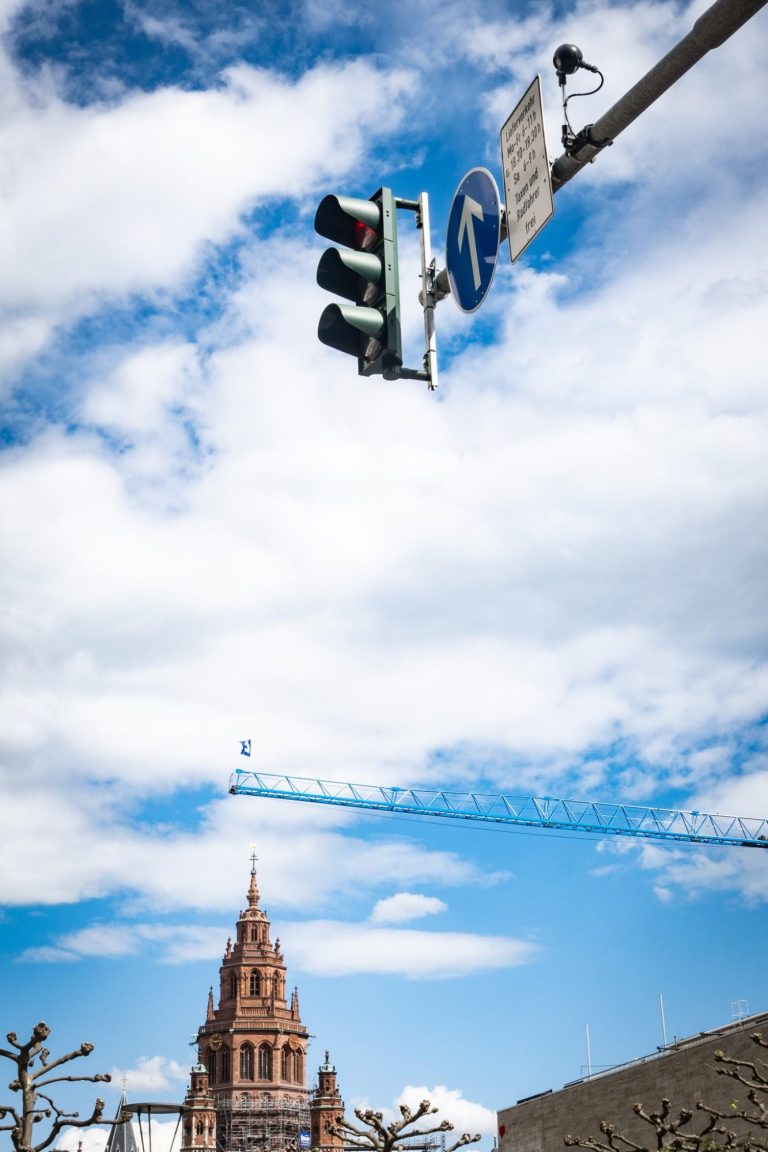 Mainzer Dom St. Martin, Ecke Weißliliengasse Grünlicht einer Ampel, im Hintergrund ein historisches Gebäude unter blauem Himmel.