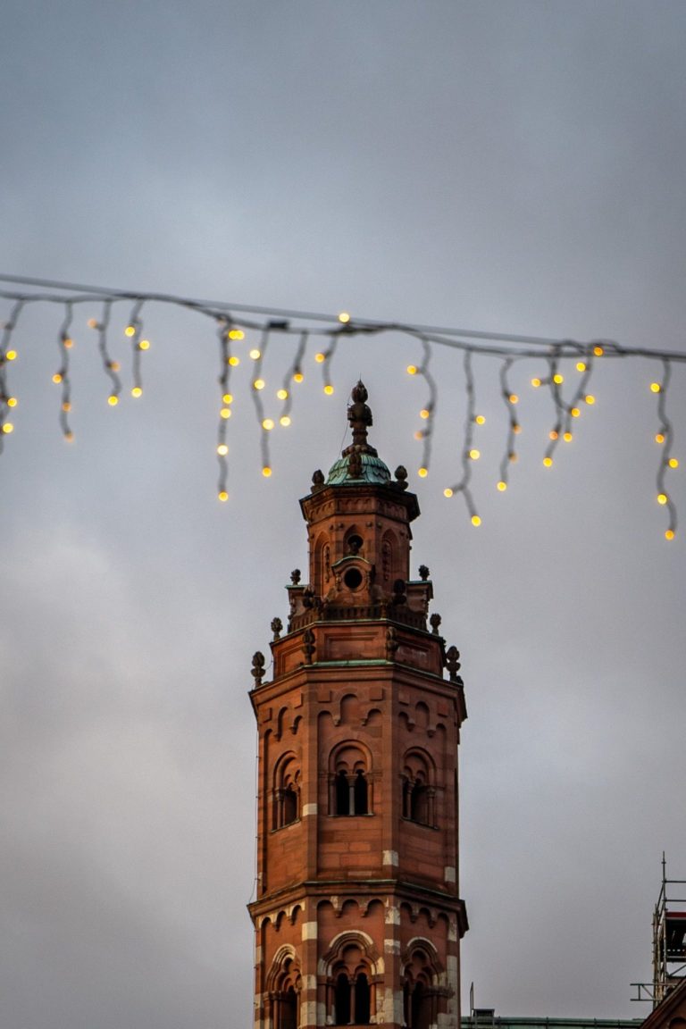 Mainzer Dom St. Martin, Weihnachtsmarkt am Leichhof Blick auf einen hohen Nebenturm des Mainzer Doms mit Lichterketten im Vordergrund zur Weihnachtszeit.